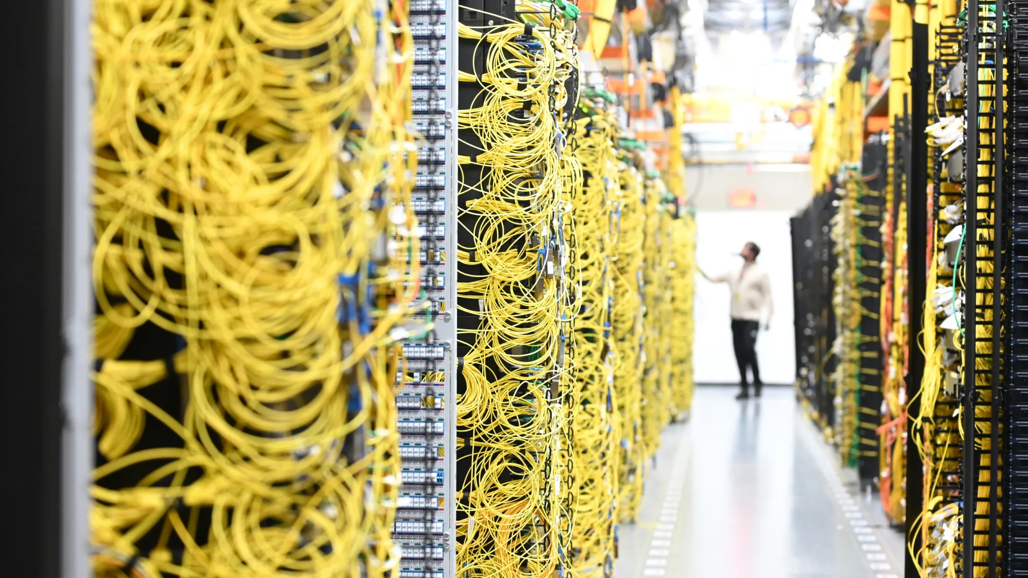 Técnico en el pasillo de un centro de datos de Amazon, entre racks de servidores llenos de cables de red amarillos